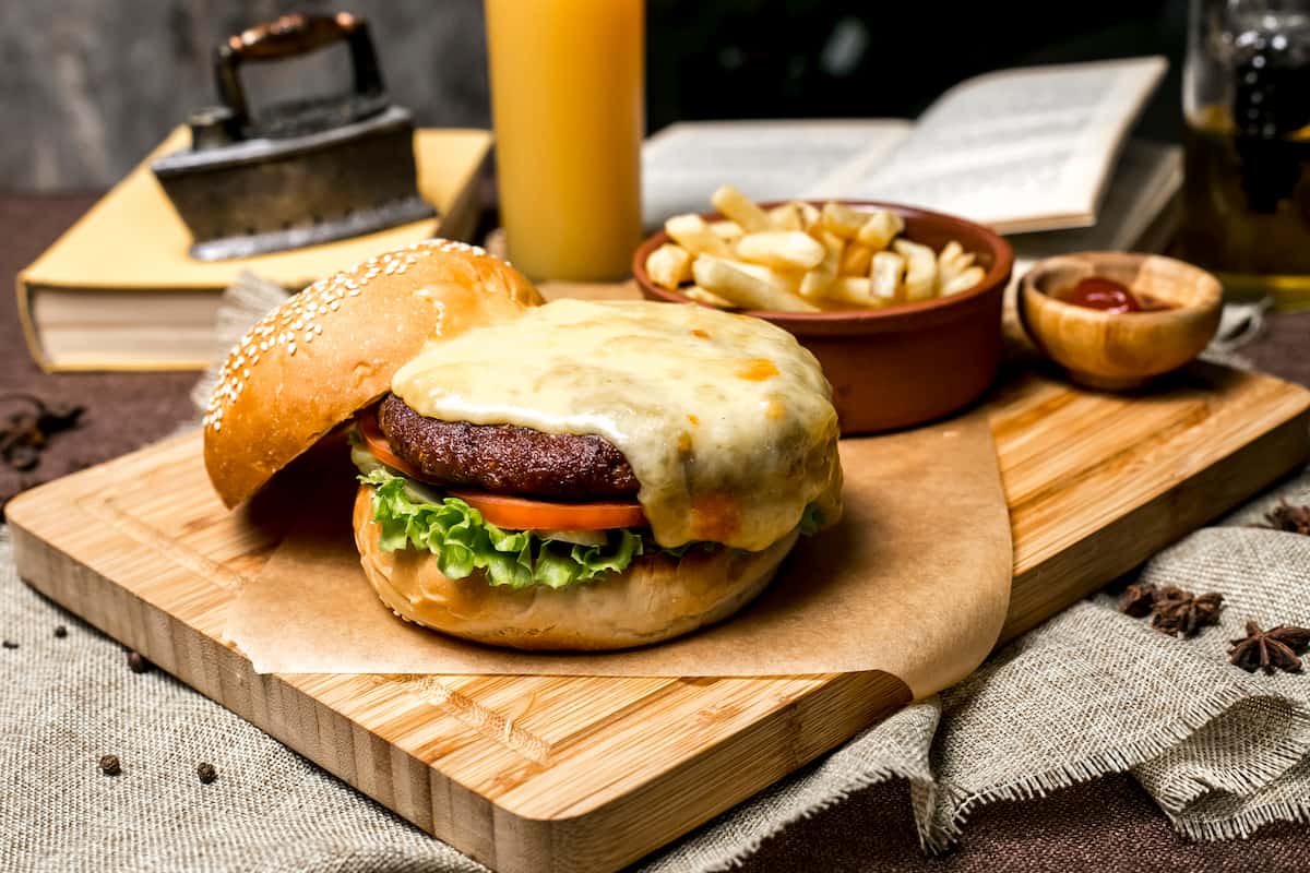 Hamburguesa con queso y papas fritas sobre tabla de madera, ideal para ilustrar estrategias para delivery de sándwiches.