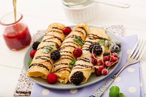 Deliciosos crepes franceses adornados con moras, grosellas y salsa de chocolate. Exquisita comida francesa para el desayuno.