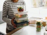 La imagen presenta a una persona trabajando sobre una mesa con diferentes prototipos de empaques, planos técnicos y material visual. Aunque a primera vista parece centrada en el diseño de packaging, también representa una etapa clave en la optimización del menú de una dark kitchen: el desarrollo estratégico de productos y presentación para delivery.