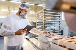 Profesional en una cocina profesional, utilizando una tableta y vistiendo ropa de protección, organizando productos.