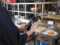 La imagen muestra a una persona vestida con un uniforme de chef negro, de pie en lo que parece ser una cocina profesional o industrial. 