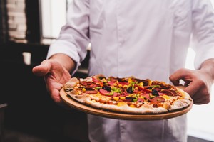 Pizzero sosteniendo una pizza recién horneada, listo para servir en una pizzería tradicional y simbolizando cómo montar una pizzería.