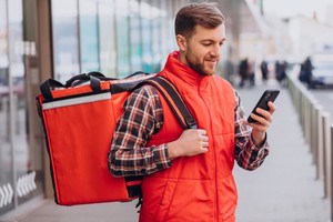 Repartidor revisando su celular mientras usa una mochila térmica, ideal para ilustrar sobre aplicaciones para hacer delivery.