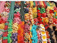 La imagen muestra una colorida y abundante variedad de golosinas dispuestas de manera ordenada. Hay gomitas de muchas formas y sabores: ositos, corazones, huevos fritos, delfines, serpientes, estrellas, fresas, pizzas en miniatura, entre otras figuras divertidas.