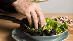 sta imagen muestra a un chef preparando una ensalada en una cocina profesional.