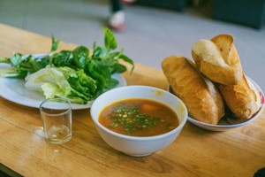 Plato con sopa, plato con pan francés y plato con ensalada. Al lado, un vaso vacío.