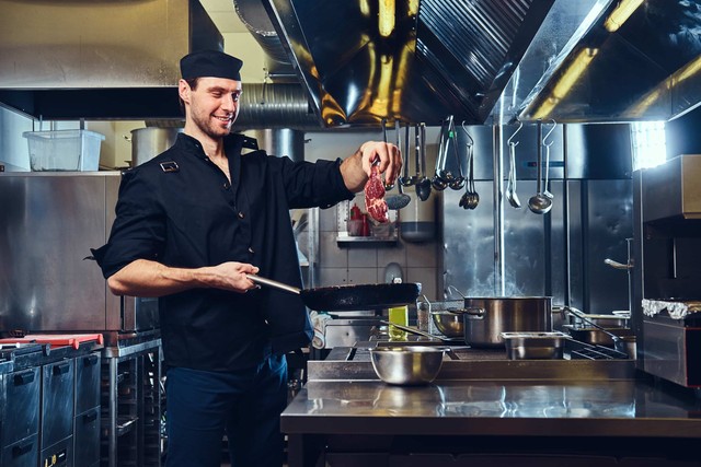 cocina en casa: el chef sostiene carne de cerdo debajo de la sartén en la cocina