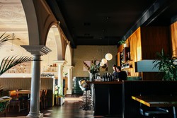 El interior de un restaurante moderno y elegante con arcos decorativos y columnas a la izquierda, dividiendo los espacios.