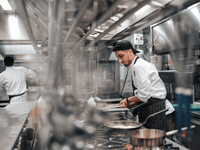 La imagen muestra a dos chefs trabajando en una cocina profesional con una atmósfera ajetreada y moderna.