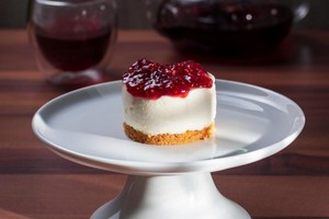 Delicioso postre para vender de cheesecake con base de galleta, crema blanca y cobertura roja.