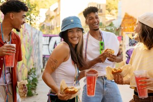Jóvenes disfrutan de hamburguesas y bebidas al aire libre, aprovechando ofertas de comida durante festivales urbanos.