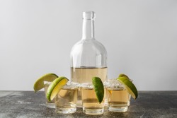 Dos vasos altos de cócteles con pisco, decorados con rodajas de lima fresca y hojas de menta. Los vasos están rodeados de cubos de hielo y limas, sobre una superficie de mármol claro.