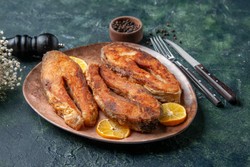 Tres filetes de pescado fritos servidos en un plato de cerámica marrón, decorados con rodajas de limón fresco.